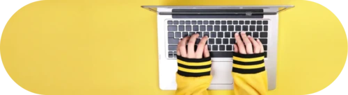 Hands wearing striped sleeves typing on a laptop against a bright yellow background.