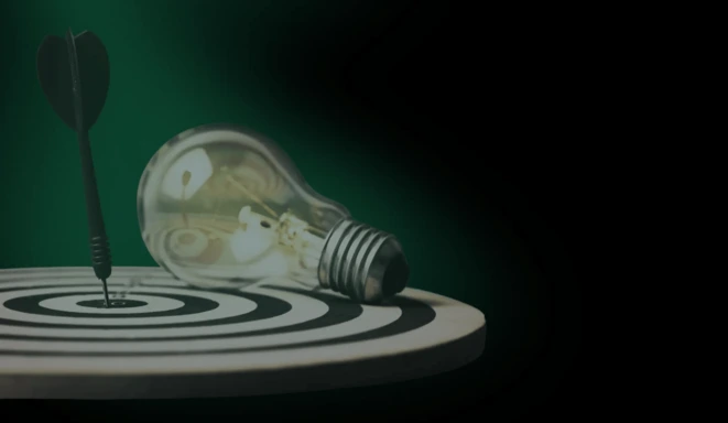 A dart hitting the bullseye on a black-and-white target with a lightbulb lying next to it, symbolizing precision and innovative ideas against a green background.